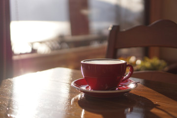 A cup of coffee put on the wood table, background is a lake in a chiny day