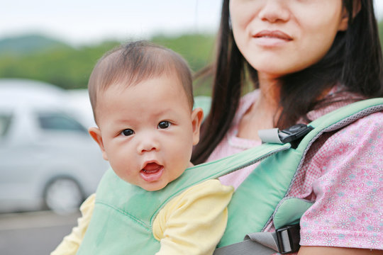 Close-up mother carrying her infant by ergonomic baby carrier.