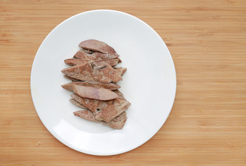Boiled meat pork liver in white plate on wooden board background with copy space.