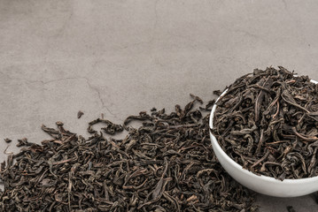 Dried tea is poured into a white ceramic cup on a gray textured background.