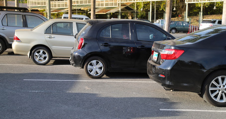 Closeup of back or rear side of black car and other cars parking in parking lot with natural background in bright sunny day. 