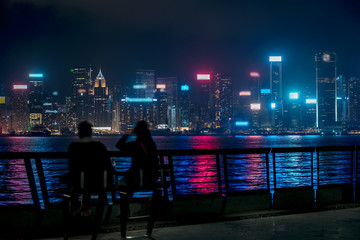 Hong Kong cityscape at night. Tourists walking on the waterfront