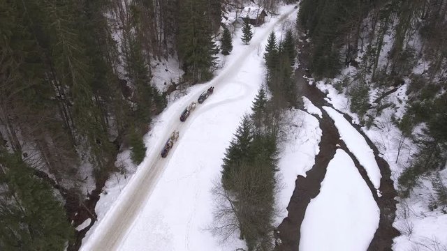Aerial shot of tree horse teams pulling sleigh in a narrow mountain valley during late winter