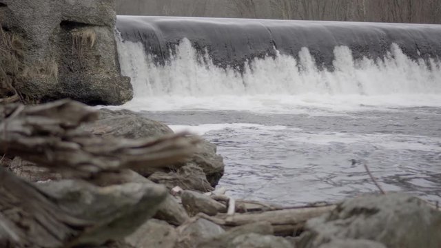 deadwood tree trunk washed up along a rocky river bank with cascading water overlfowing a check dam