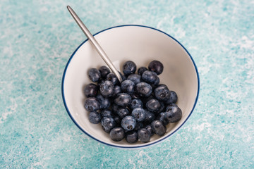 Blueberries in a bowl on a turquoise background.