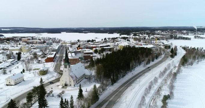 Lapland village, C4k aerial, drone shot, of Kemijarvi church and the town, over road e63, towards a lake, in nordic wilderness, on a overcast, winter day, at the arctic circle, in Lapland, Finland