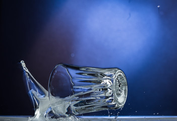 Falling and jumping glass with spilling liquid on a blue gradient background