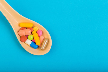 Colorful medical pills on spoon and capsules or supplements for therapy in background, concept of treatment and health care