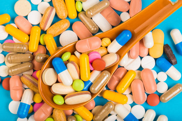 Colorful medical pills on spoon and capsules or supplements for therapy in background, concept of treatment and health care