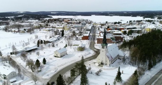 Lapland village, C4k aerial, reverse, drone shot, of Kemijarvi church and the town, road e63 and a lake, in nordic wilderness, on a cloudy, winter day, at the arctic circle, in Lapland, Finland