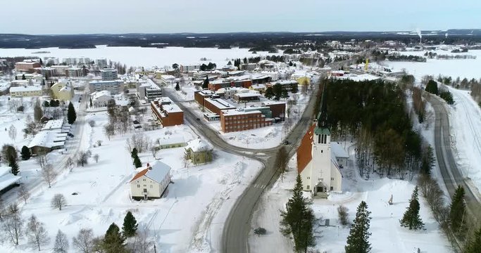 Lapland village, C4k aerial, tracking, drone shot, of Kemijarvi church and the town, road e63 and wilderness, on a cloudy, winter day, at the arctic circle, in Lapland, Finland