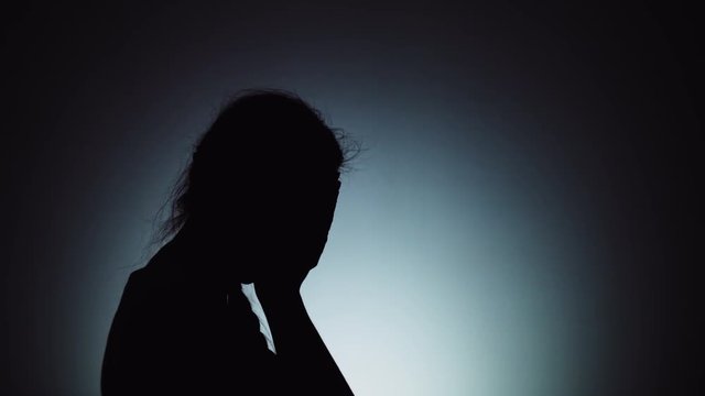 Silhouette of a woman. The shadow of a woman on a light background. A woman is crying, covering her face with her hands. Emotions, crying.