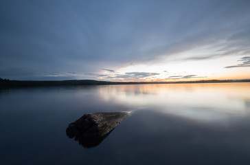 Rock in a calm lake in sweden at sunset
