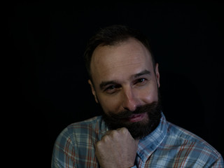Fototapeta premium a man with a beard and mustache with a thoughtful sly face on a black background
