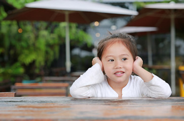 Smiling little Asian child girl lying on the wooden table with looking out.