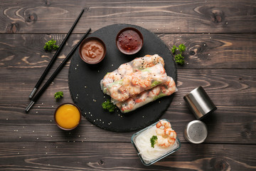Slate plate with tasty spring rolls on wooden table