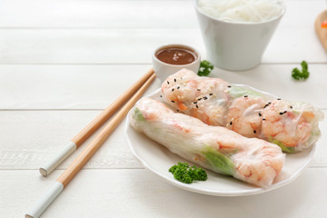 Plate with tasty spring rolls on white table