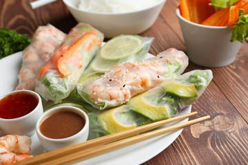 Plate with tasty spring rolls and sauces on wooden table