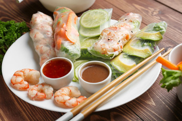 Plate with tasty spring rolls and sauces on wooden table
