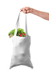 Female hand holding eco bag with products on white background