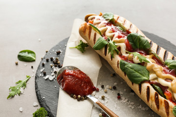 Tasty hot dog with sauce on slate plate, closeup