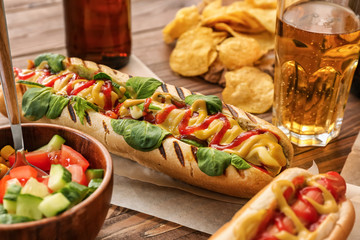 Tasty hot dogs with beer and vegetable salad on wooden table