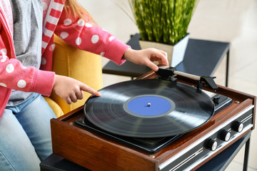 Cute little girl listening to music through record player at home