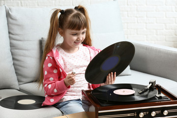 Cute little girl listening to music through record player at home