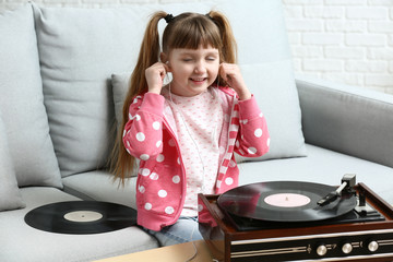 Cute little girl with earphones listening to music through record player at home