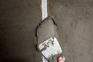 Plasterer sealing joint of building wall with putty knife.