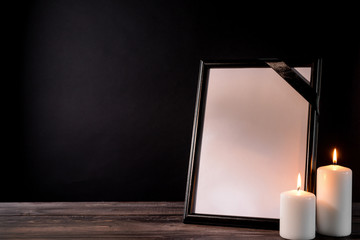 Blank funeral frame and candles on table against black background