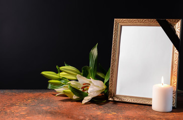 Blank funeral frame, candle and flowers on table against black background