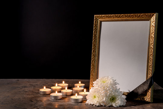 Blank Funeral Frame, Candles And Flowers On Table Against Black Background