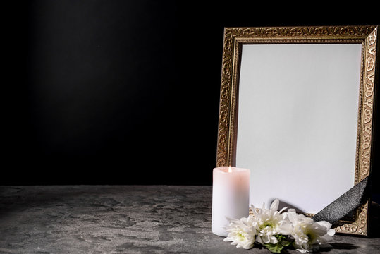 Blank Funeral Frame, Candle And Flowers On Table Against Black Background