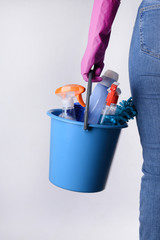 Woman with set of cleaning supplies on light background