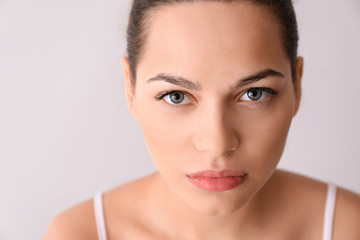 Beautiful young woman with eyelash extensions on light background