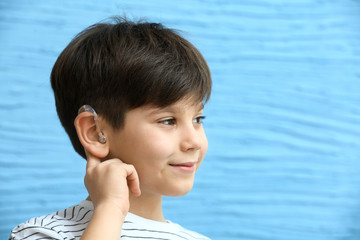 Little boy with hearing aid on color background