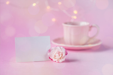 Obraz na płótnie Canvas Coral rose with blank card and cup of tea on pink background with bokeh. Postcard concept. Happy Mother's Day, Women's Day or Birthday. Minimalism, selective focus, close-up.
