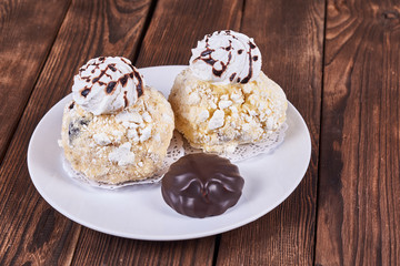 Two airy desserts with meringue in chocolate drops with prunes and butter cream and the chocolate zephyr in a white plate on a wooden background