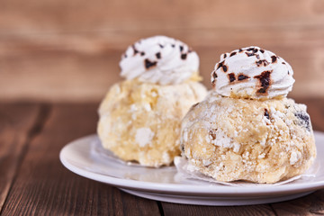 Two airy desserts with meringue in chocolate drops with prunes and butter cream in a white plate on a wooden background