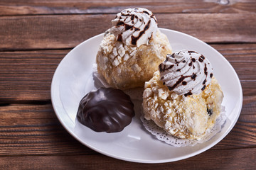Two airy desserts with meringue in chocolate drops with prunes and butter cream and the chocolate zephyr in a white plate on a wooden background