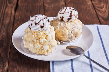 Two airy desserts with meringue in chocolate drops with prunes and butter cream and napkin on a wooden background