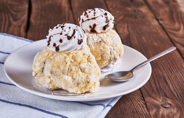 Two airy desserts with meringue in chocolate drops with prunes and butter cream in a white plate and napkin on a wooden background