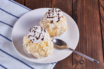 Two airy desserts with meringue in chocolate drops with prunes and butter cream in a white plate and napkin on a wooden background