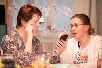 Two women discussing something while holding a smartphone in their hands while sitting at home at the holiday table
