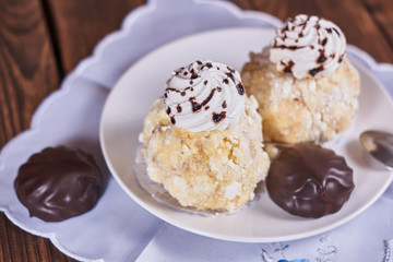 Two airy desserts with meringue in chocolate drops with prunes and butter cream and the chocolate zephyr in a white plate on a wooden background