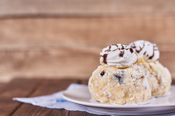 Two airy desserts with meringue in chocolate drops with prunes and butter cream next to napkin on a wooden background. Close-up
