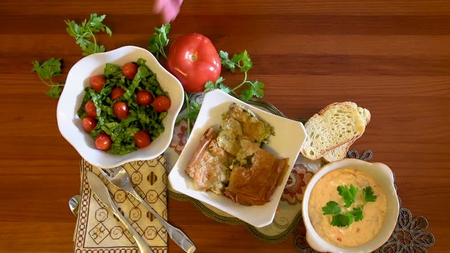 Healthy mediterranean cuisine, three dishes concept for lunch or dinner. Closeup of placing a tomato next to the letuce salad on the table