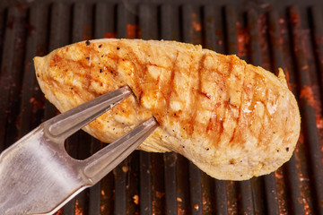 Grilled cooking. Cook checks for readiness with a fork in chicken breast.