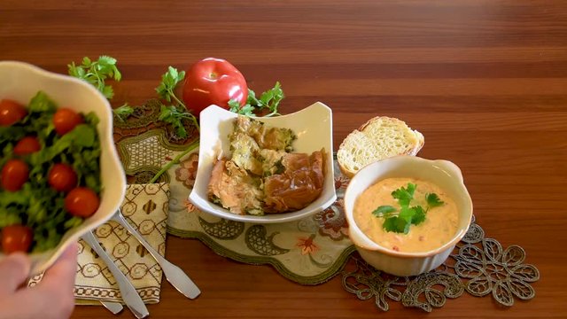 Healthy mediterranean cuisine, three dishes concept for lunch or dinner. Side view closeup of placing the letuce salad on the table in slow motion